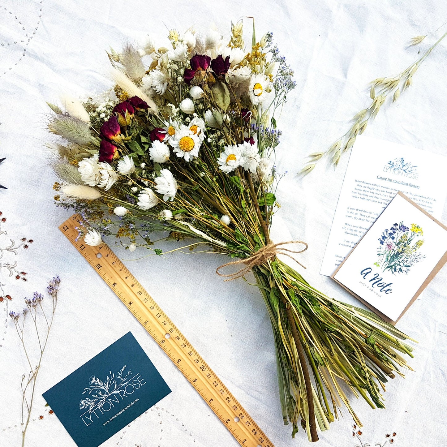 The dried flower bouquet is laid on a white linen background next to a twelve inch ruler. You can see it is a few inches longer than the ruler.