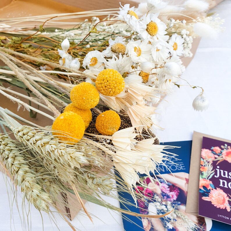 Dried Flower Mixed Box of Meadow Style Loose Stems- the arrangement is called Summer Gold by Lytton Rose Botanical. A cardboard box filled with a vibrant assortment of dried flowers and grasses. The flowers include white daisies, gypsophila and yellow craspedia, while the grasses feature a mix of wheat, oats and fluffy lagurus bunny tails.