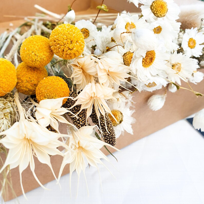 Dried Flower Mixed Box of Meadow Style Loose Stems- the arrangement is called Summer Gold by Lytton Rose Botanical. A cardboard box filled with a vibrant assortment of dried flowers and grasses. Image shows a close up of white daisies, nigella orientalis and yellow craspedia.