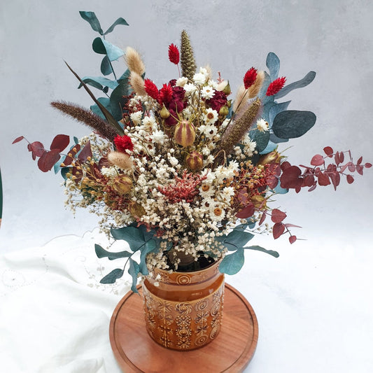 "Winter Woodlands" Preserved Eucalyptus & Dried Roses Bouquet - Lytton Rose Botanical. A brown ceramic vase (not included) filled with a vibrant bouquet of dried flowers. The bouquet features a mix of white gypsophila, red roses, burgundy and green eucalyptus leaves. The vase is displayed on a wooden tray.