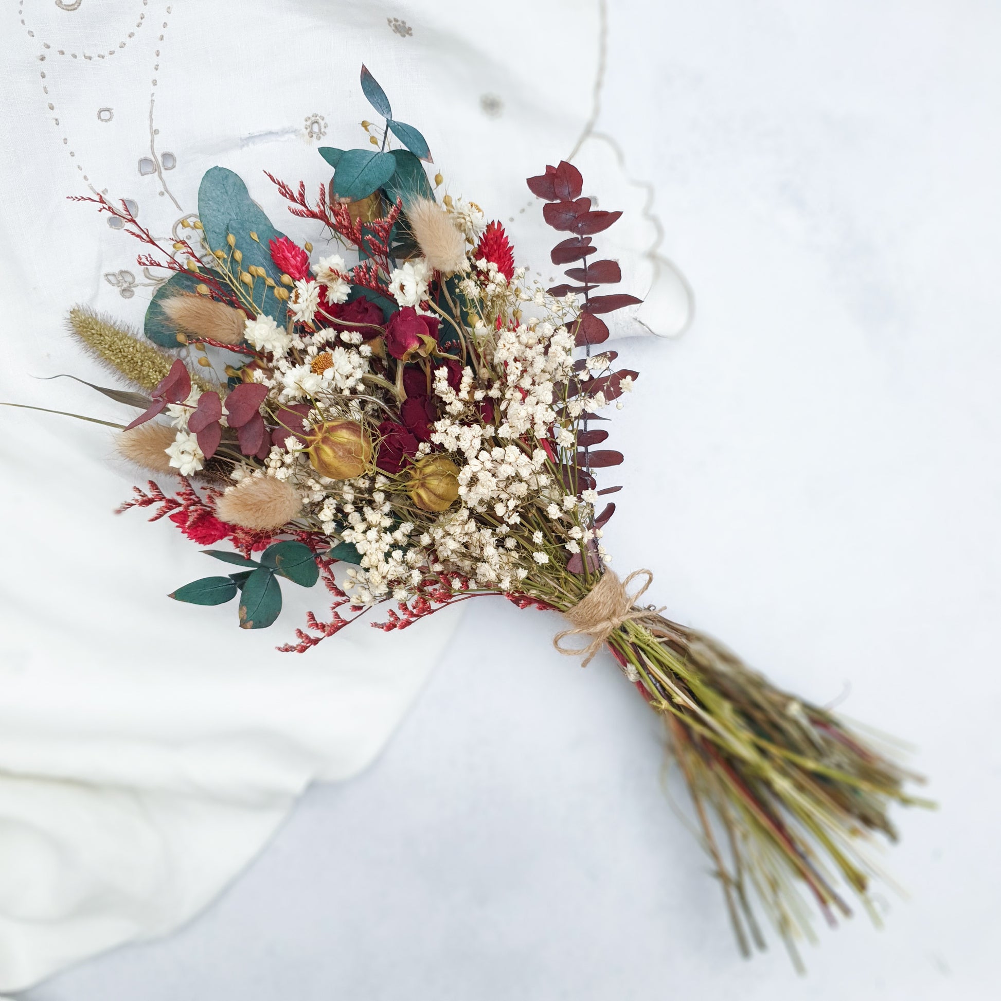 "Winter Woodlands" Preserved Eucalyptus & Dried Roses Small Bouquet - Lytton Rose Botanical. A beautifully arranged bouquet of dried flowers, showcasing a mix of white gypsophila, red roses, and green eucalyptus leaves. The arrangement also includes dried roses and grasses for added texture. The posy is elegantly bound with twine.