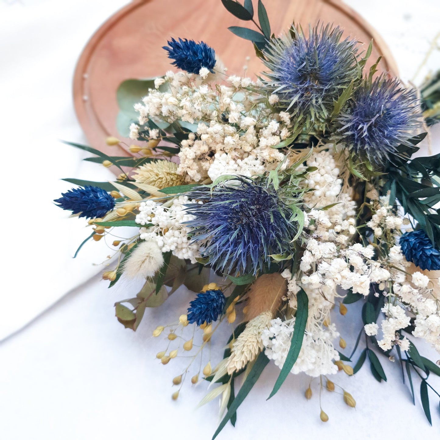 "Frosted Forest" Dried and Preserved Small Eucalyptus Bouquet - Lytton Rose Botanical. Close up of a  beautifully arranged bouquet of dried flowers. Delicate white flowers, vibrant blue thistles, and lush green eucalyptus leaves create a stunning contrast.